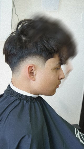 Profile view of a person with a modern undercut hairstyle, showing short faded sides and longer dark hair on top, wearing a barber cape