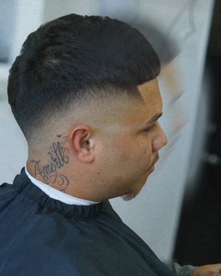 Side profile of a man with a modern fade haircut, black cape, and neck tattoo