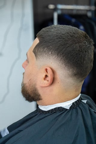 Side profile of man with short fade haircut and beard wearing black barber cape
