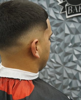 Side profile of a person with a short fade haircut wearing a red and black shirt at a barber shop