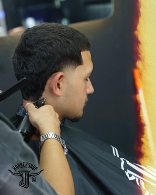 Man in profile at barbershop wearing black cape with clippers near ear, showing fresh fade haircut