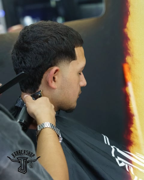 Man in profile at barbershop wearing black cape with clippers near ear, showing fresh fade haircut