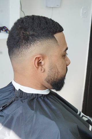 Man with a fade haircut and beard, shown in profile view wearing a black barber cape