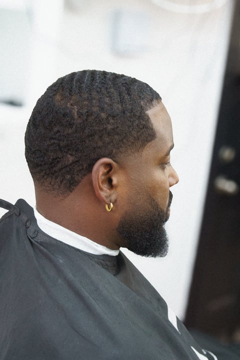 Profile view of a man with short textured hair and beard, wearing a black shirt with white collar detail