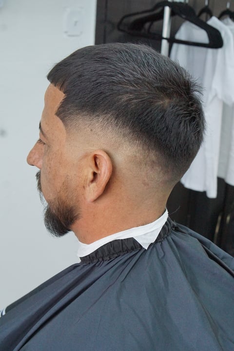 Man with fade haircut and beard wearing barber cape in salon setting